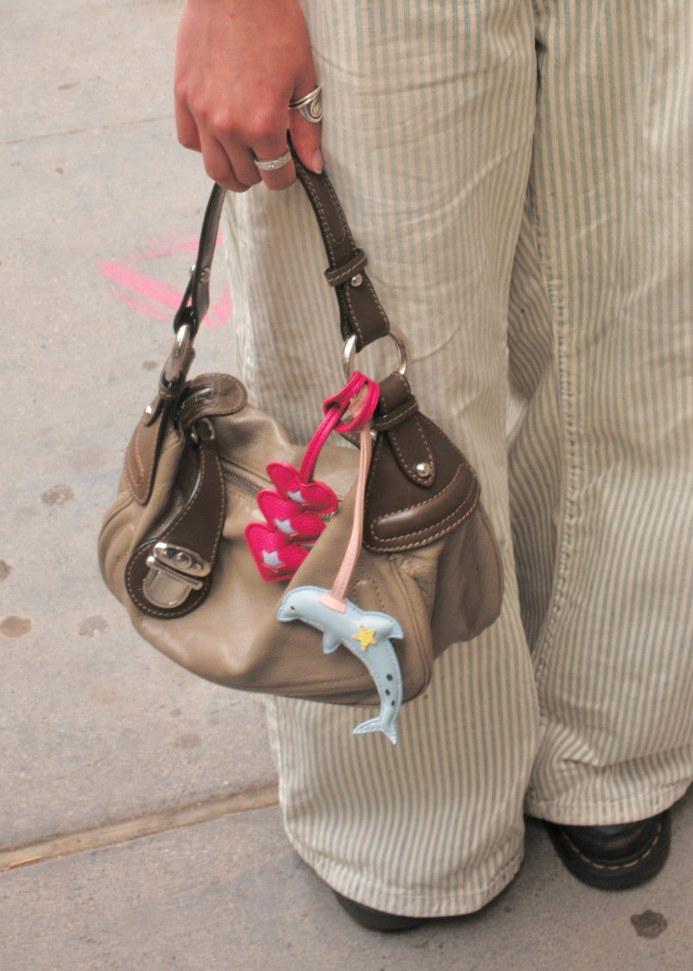 Person holding a brown handbag with colorful keychains on a sidewalk.