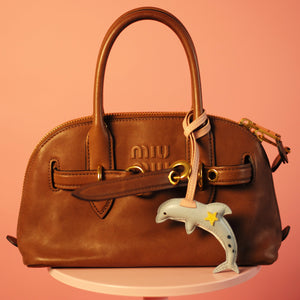 Brown handbag with a decorative charm on a pink background