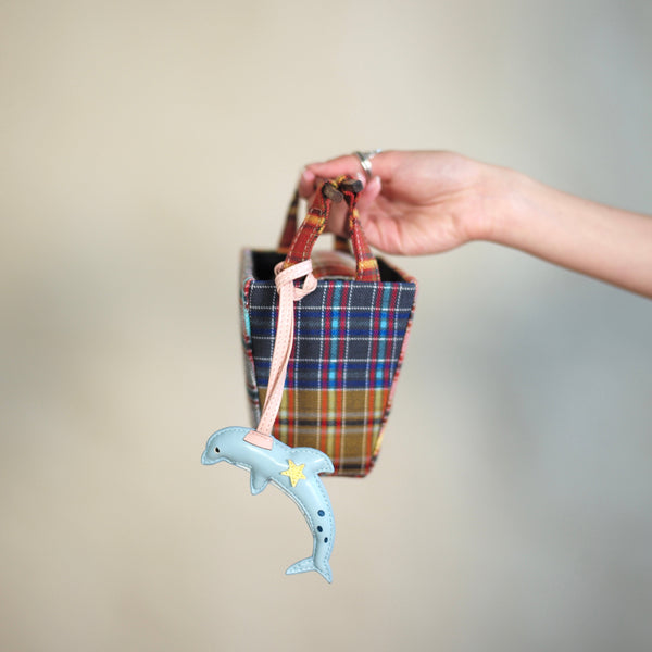 Hand holding a plaid bag with a dolphin toy on a plain background